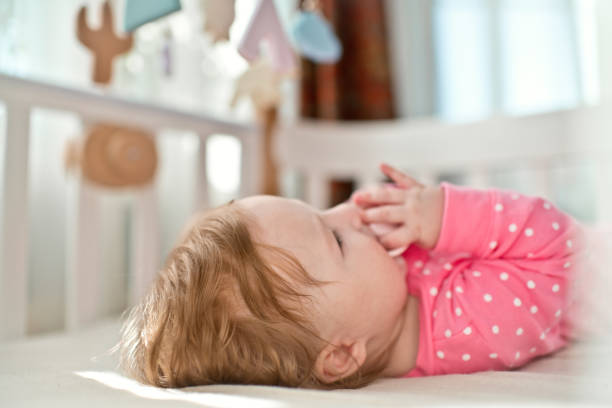 a baby laying on a bed while holding on the pacifier  in her mouth
